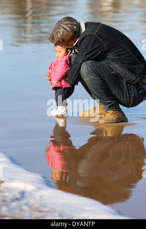 Padre coying oltre il toddler figlia su un wet spiaggia sabbiosa a Essaouira, Marocco, non vedendo un'onda in arrivo fino a molto ultimo minu Foto Stock