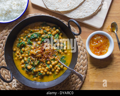 Ceci e spinaci curry con cipolle caramellate, riso, chapatis e chutney di mango su un tavolo in legno di quercia Foto Stock