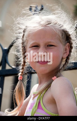 Closeup ritratto di sorridente bambina con lunghi biondi pigtail guardando la fotocamera Foto Stock