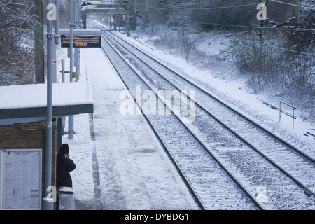 Un vuoto National Express linea ferroviaria ad una coperta di neve sobborgo stazione con una persona in piedi sulla piattaforma in Essex, Foto Stock