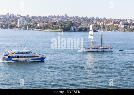 Traghetto nel porto di Sydney passando un brigantino veliero. Foto Stock