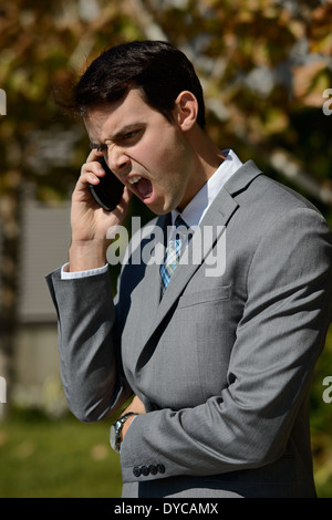 Un giovane uomo di affari in business suit gridando rabbiosamente in il suo telefono cellulare. Un ritratto arrabbiato concetto. Foto Stock