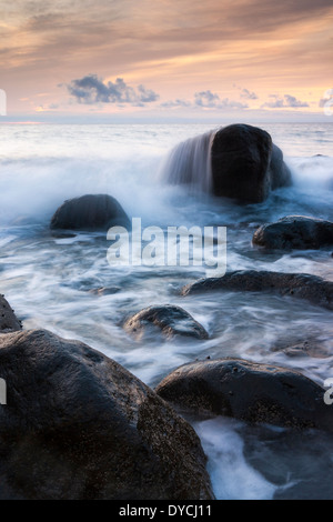 Onde che si infrangono su grossi massi al tramonto sulla costa nord di Gran Canaria Isole Canarie Spagna. Foto Stock