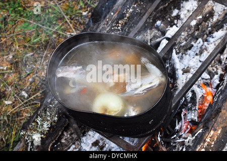 Pentola su un cavalletto in piedi sopra il fuoco. La preparazione di una zuppa di pesce sul fuoco durante il viaggio. Foto Stock