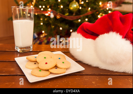 Piastra di biscotti frollini con un bicchiere di latte e di Santa hat Foto Stock