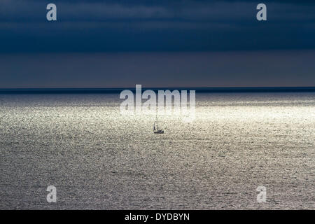 Un piccolo yacht a vela lontano fuori in mare. Foto Stock