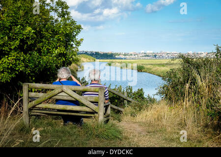 Un giovane seduto su una panca in legno godendo la vista oltre a Southend. Foto Stock