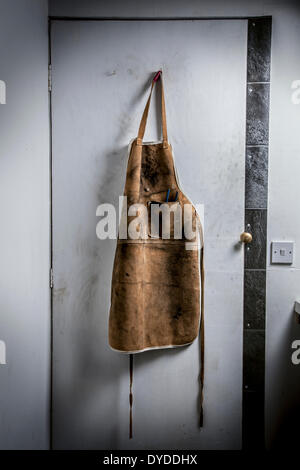 Workshop di cuoio grembiule appeso su una porta di officina. Foto Stock