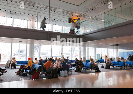 I passeggeri in attesa in un aeroporto partenza lounge al di sotto di un corridoio di arrivi. Foto Stock