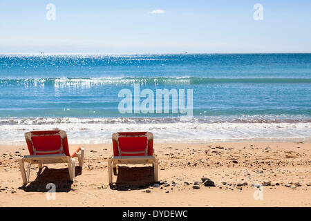 Due rosso non occupato sedie a sdraio sulla spiaggia dal mare. Foto Stock
