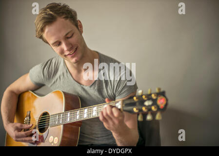 Un bel giovane uomo suonare la chitarra acustica. Foto Stock