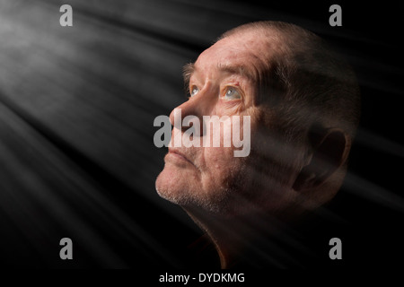 Il vecchio uomo senior cercando di pregare al buio in raggi di luce Foto Stock