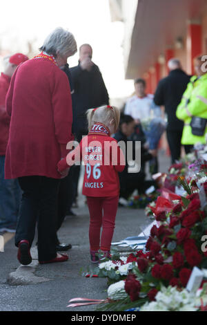 Liverpool, Regno Unito. Il 15 aprile 2014. Una giovane ragazza che indossa una maglietta di Liverpool guarda a fiori e omaggi sinistro esterno Anfield. Migliaia di persone si erano raccolte per rendere omaggio al 96 i tifosi di calcio che morì nel 1989. Credito: Adam Vaughan/Alamy Live News Foto Stock