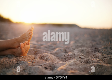 Primo piano immagine di piedi della vecchia donna seduta rilassante sulla spiaggia sabbiosa. Foto Stock