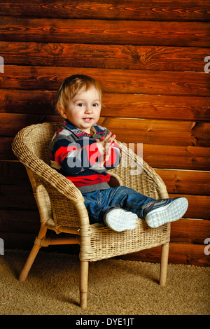 Piccolo Ragazzo seduto in una sedia di vimini in una casa in legno Foto Stock