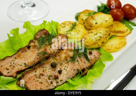 Due pezzi di pancetta fritta su una foglia di insalata. Fette di patate arrosto e prezzemolo con aneto e spezie. Tre pomodori sott'aceto Foto Stock