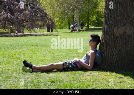 Giovane uomo seduto contro albero in sole in Hyde Park. Foto Stock