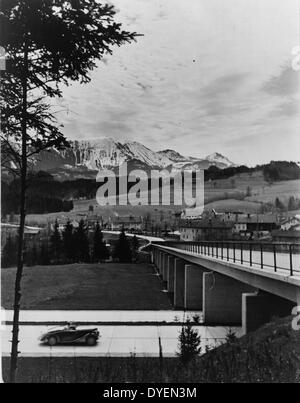 Automobile avvicinando cavalcavia sulla autostrada Autobahn (autostrada) con vista della campagna e le montagne sullo sfondo. datati tra il 1936 e il 1939. Foto Stock