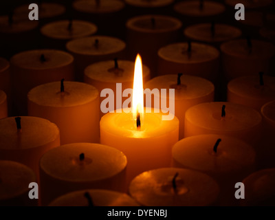 Un sacco di candele accese di notte con un solo acceso Foto Stock