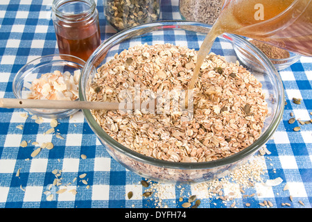 Rendendo granola muesli e cereali misti, semi e noci in una terrina versare liquidi sulla, blu e bianco sullo sfondo di controllo (5 di 26) Foto Stock