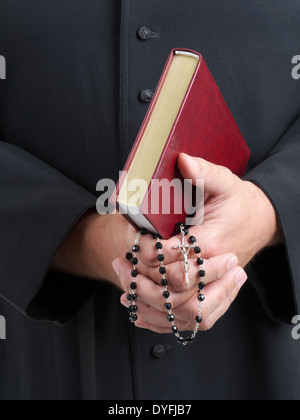 Primo piano di un sacerdote cattolico di mani tenendo la Sacra Bibbia e il rosario Foto Stock