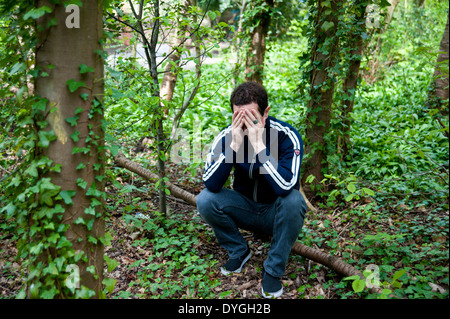 Un uomo depresso sedersi da solo nei boschi con testa in mani Foto Stock