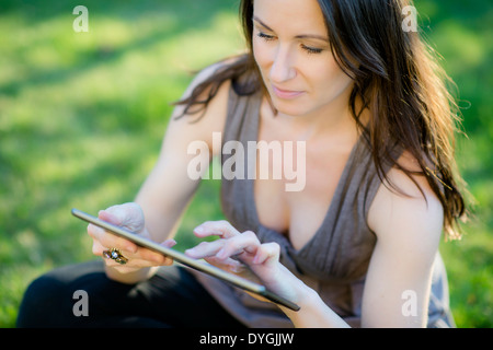 Frau sitzt mit Tablet in der Wiese - donna con la compressa nel prato Foto Stock