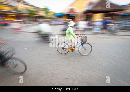 Donna asiatica di equitazione Bicicletta blu. Persona sulla bicicletta. Il bivio di Hoi An in Vietnam, in Asia. La sfocatura movimento della strada trafficata con case. Foto Stock