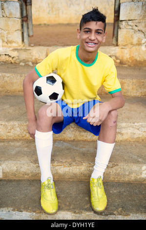 Sorridente Ritratto di giovane brasiliano giocatore di calcio calcio holding seduti all'aperto nella sua favela di quartiere Foto Stock