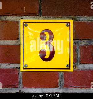 Casa smaltato numero tre. Lettering marrone su sfondo giallo. Foto Stock