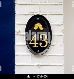 Metallo colato numero di casa quaranta tre. Dipinto di nero e giallo su una targhetta ovale con scarpe di legno. Foto Stock