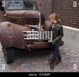 Giovane ragazza bionda in piedi di fronte a un vintage rusty Dodge carrello Foto Stock