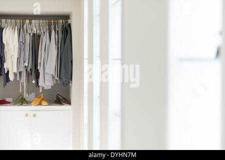 Fila di nuovo abbigliamento casual su appendiabiti in negozio con quattro coloratissimi paia di scarpe al di sotto di esso. Abbigliamento presentato come nel guardaroba. Foto Stock