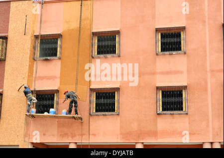 Pittori pittura dalla piattaforma della puleggia al di fuori dei nuovi edifici di appartamenti nella periferia di Marrakech, Marocco Foto Stock