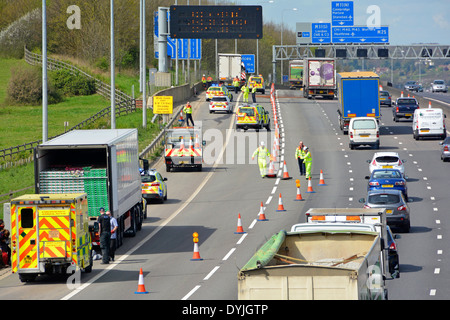Gli uomini lavorano sui coni che riaprono parte dell'autostrada M25 dopo un incidente a distanza + incidente in corso di ricerca di camion della polizia più vicino a Essex UK Foto Stock