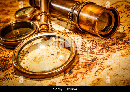 Vintage lente di ingrandimento, bussola, telescopio e un orologio da tasca giacente su una vecchia mappa. Foto Stock