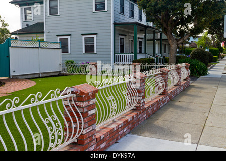 Interessante in mattoni rossi e verniciato di colore bianco in ferro battuto recinzione che circonda un cortile anteriore in Half Moon Bay, California Foto Stock