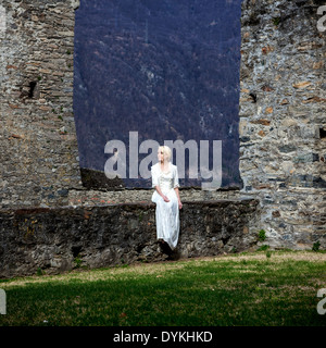 Una donna in un periodo bianco vestito è seduta su una parete in corrispondenza di un castello Foto Stock
