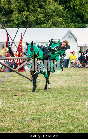 Giostre femmina cavaliere in armatura in una fiera medievale in sella ad un cavallo nero a Shugborough County evento. Foto Stock