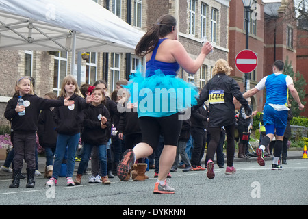 Un runner in fa tutu in primo piano corre passato Altrincham coro dei bambini nel Manchester Marathon 2014 : Foto Stock