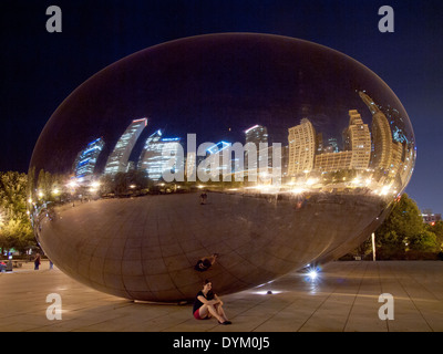 Una bella bruna ragazza si trova al di sotto del Cloud Gate (la) di fagioli in una notte d'estate del Millennium Park di Chicago, Illinois. Foto Stock