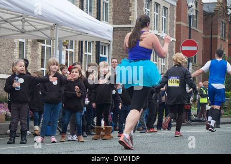 Un runner in fa tutu in primo piano corre passato Altrincham coro dei bambini nel Manchester Marathon 2014 : Foto Stock