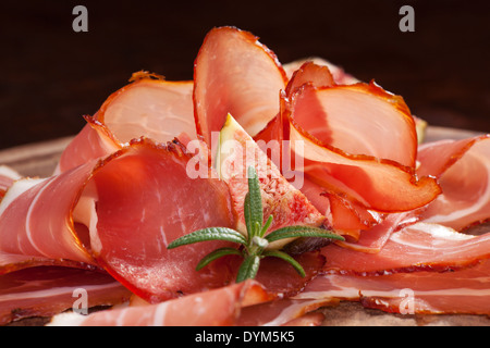 Fette di prosciutto disposta sul tagliere di legno con erbe fresche di rosmarino e di fig. Tradizionale Italiana sullo sfondo di carne. Foto Stock