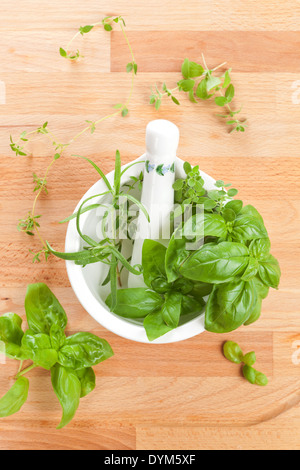 Fresche delizie aromatiche basilico, timo e rosmarino in mortaio con pestello su sfondo di legno. Vista dall'alto. Foto Stock