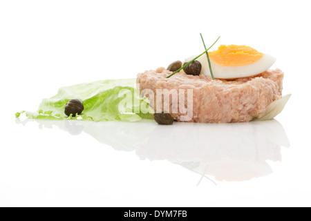 Tonno con uovo, capperi ed erba cipollina sul fresco verde foglia di insalata isolato su sfondo bianco con la riflessione. Culinario mangiare pesce. Foto Stock