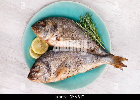 Due barbecue grigliate orata su piastra con fresche erbe di rosmarino e di limone bianco su sfondo di legno. Mediterraneo culinaria Foto Stock