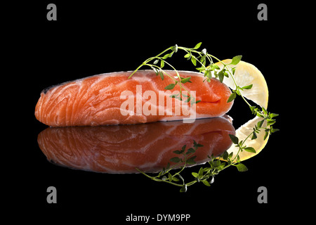 Crudo fresco bistecca di salmone con limone e timo isolati su sfondo nero con la riflessione. Lussuoso mangiare pesce. Foto Stock