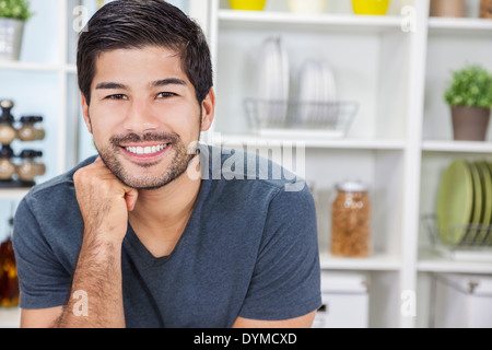 Ritratto di bello sorridente giovane uomo asiatico con la barba in una cucina a casa Foto Stock