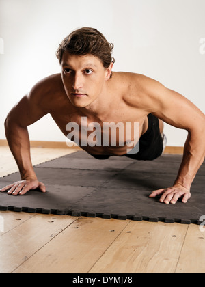 Foto di un uomo nei suoi primi anni trenta facendo pushups su un tappeto in un centro fitness. Foto Stock