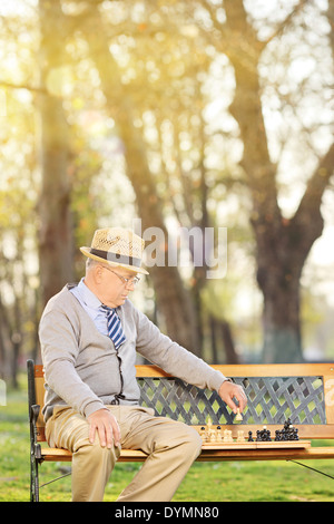 Lonely senior giocando a scacchi seduto su un banco di lavoro in posizione di parcheggio Foto Stock